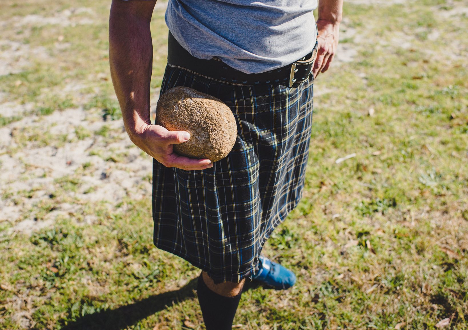 Person wearing kilt holds throwing stone in hand Highland Games Scotland