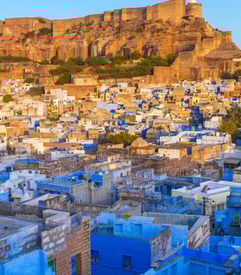 The blue city of Jodhpur with Mehrangarh Fort in the background at sunset.