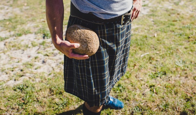 Person wearing kilt holds throwing stone in hand Highland Games Scotland