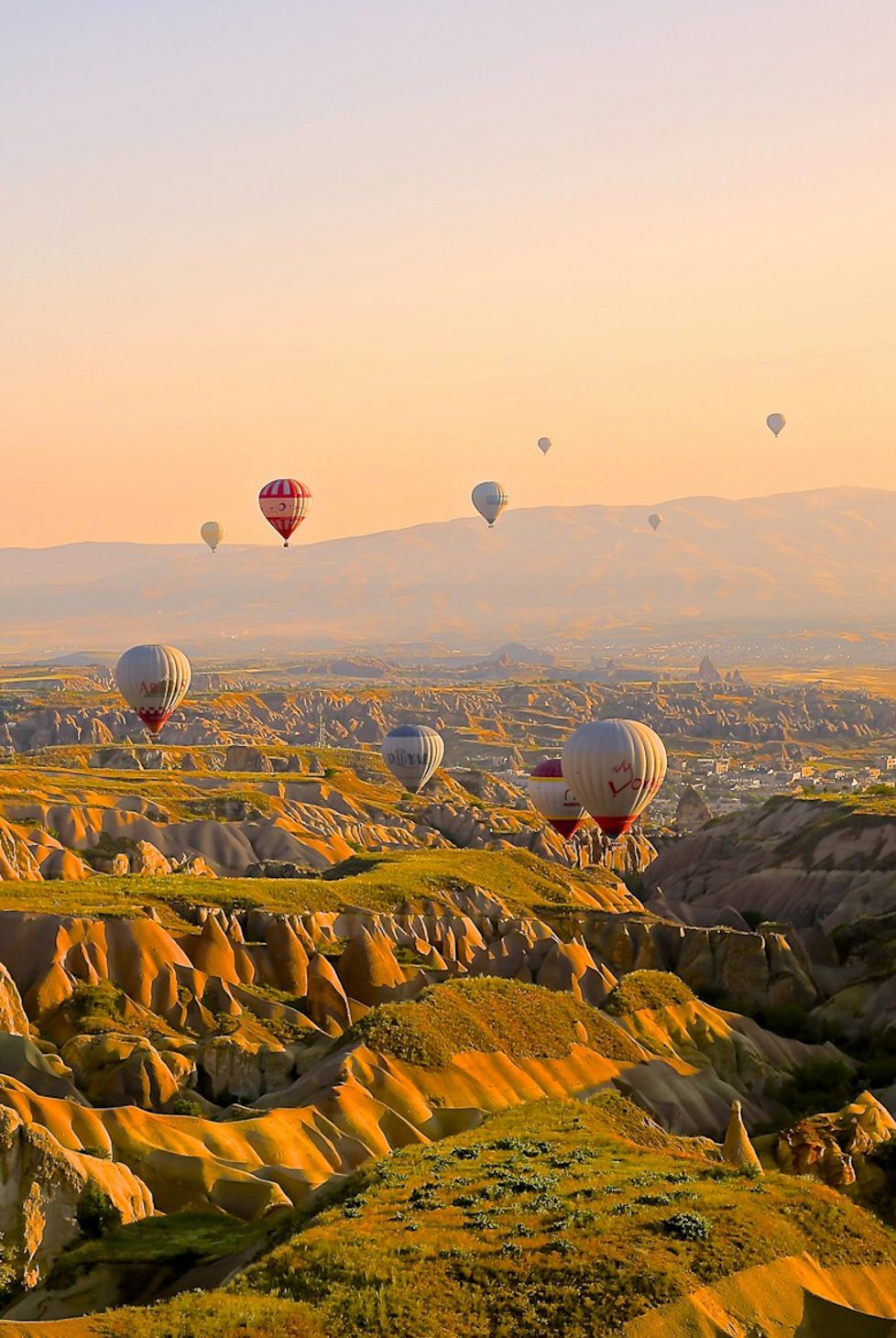 Hot air balloons float over mountainous landscapes